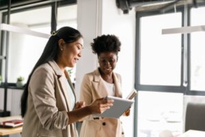 Two businesswomen looking at data on digital tablet while going on a meeting